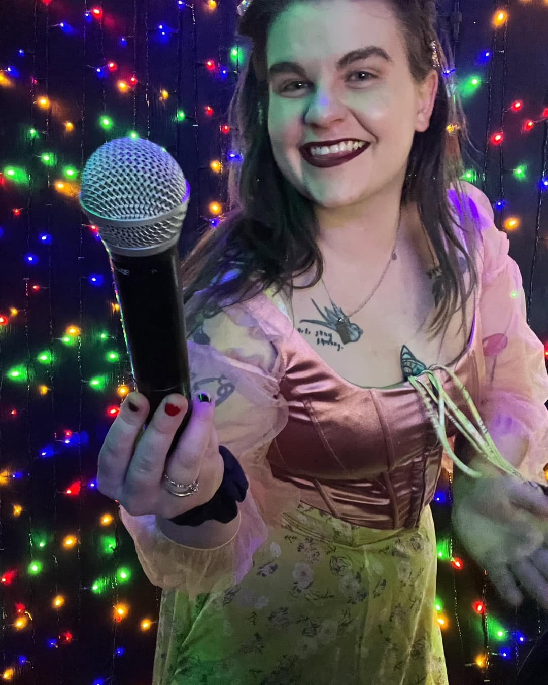 DJ Mia, a women, in a purple dress offering a microphone.